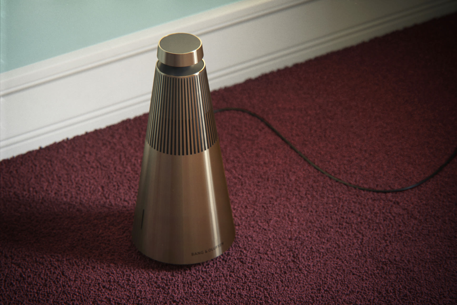 Bang & Olufsen BeoSound speaker in a copper/bronze finish on a burgundy carpet, product visualization